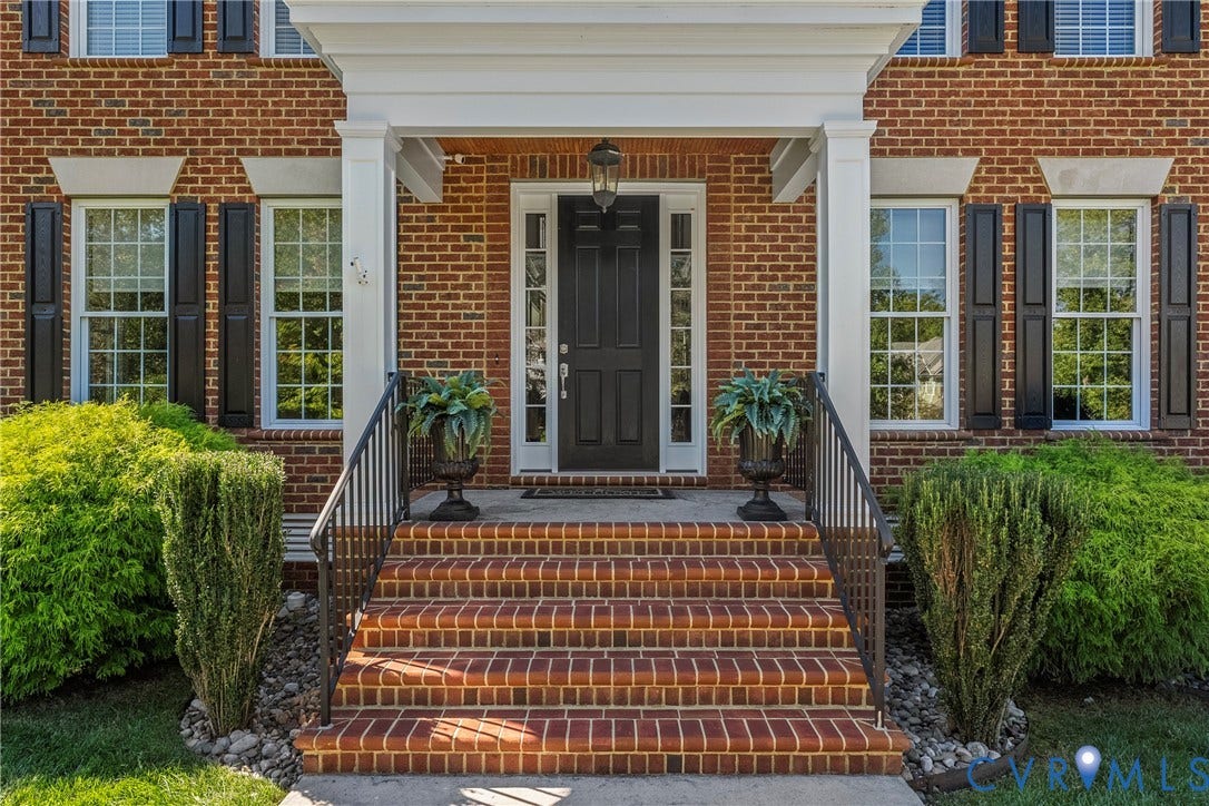 Brick facade featuring a columned portico, brick steps with wrought iron railings, and a panel door with sidelights