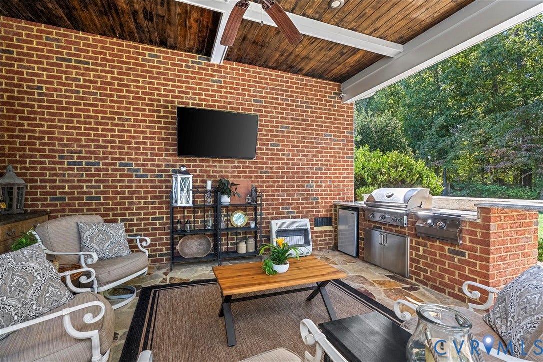 Brick exterior wall with a wood-finish ceiling, featuring an outdoor kitchen with stainless steel appliances, and a flagstone patio