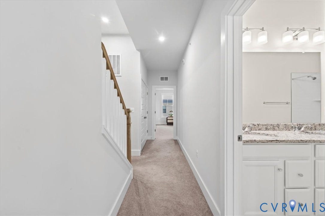 Carpeted hallway with staircase featuring natural wood handrail and white balusters