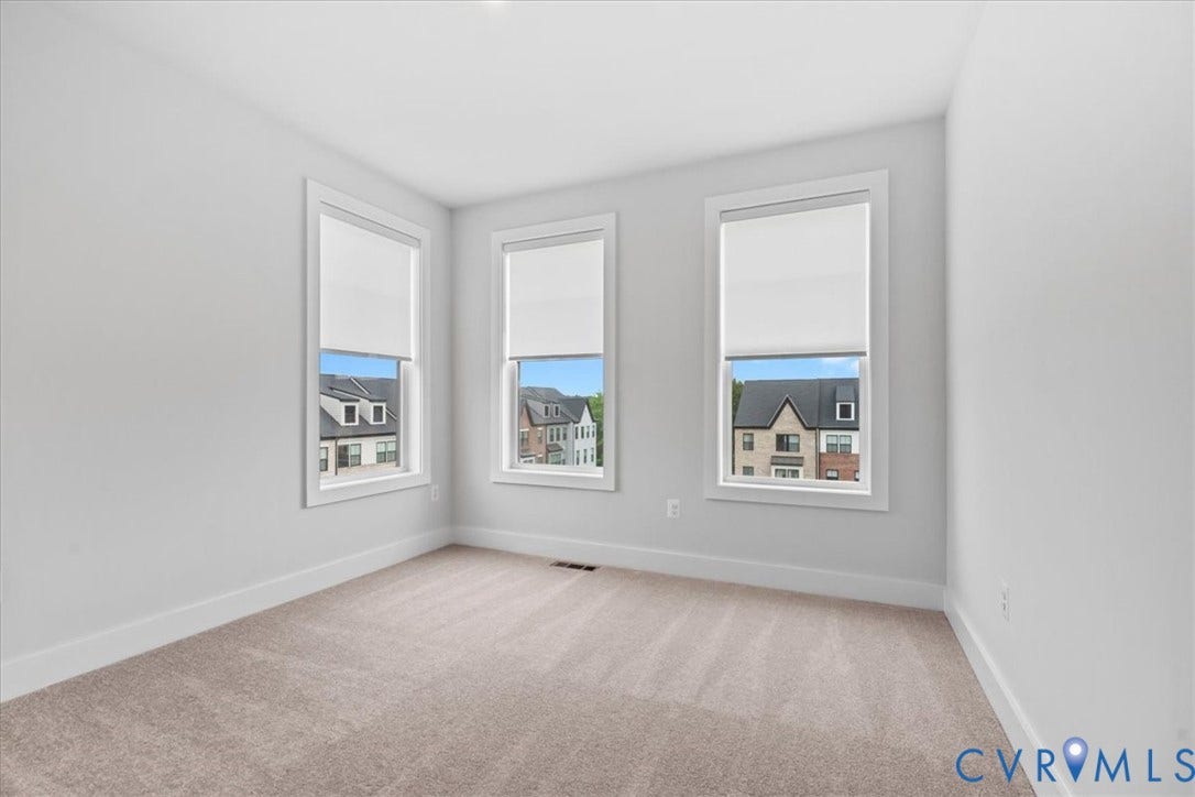 Neutral paint tones, three windows with roller shades, white window trim, and wall-to-wall carpeting