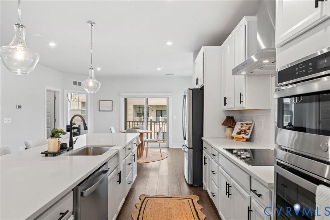 Kitchen featuring white cabinetry, stainless steel appliances, wood-finish flooring, a kitchen island with seating, and pendant lighting