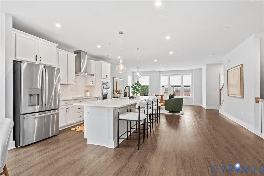 Open-concept living area featuring wood-finish flooring, a kitchen island with pendant lighting, stainless steel appliances, white cabinetry, and recessed lighting