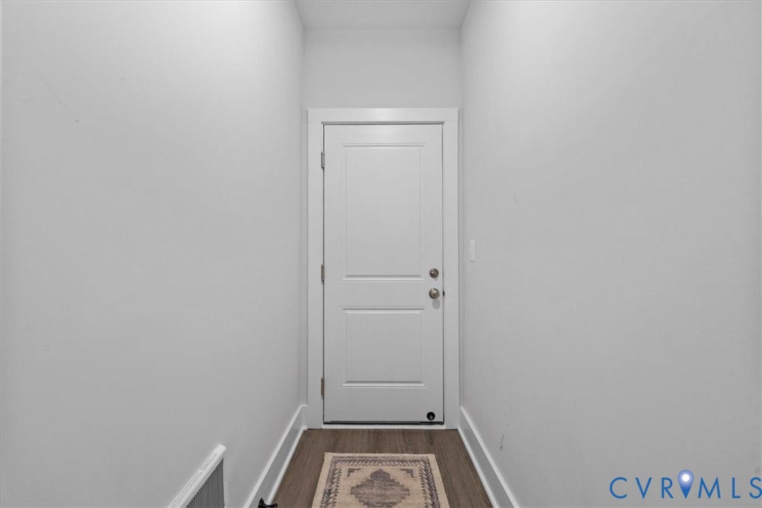 Recessed entryway with a paneled door, light-toned walls, and wood-finish flooring
