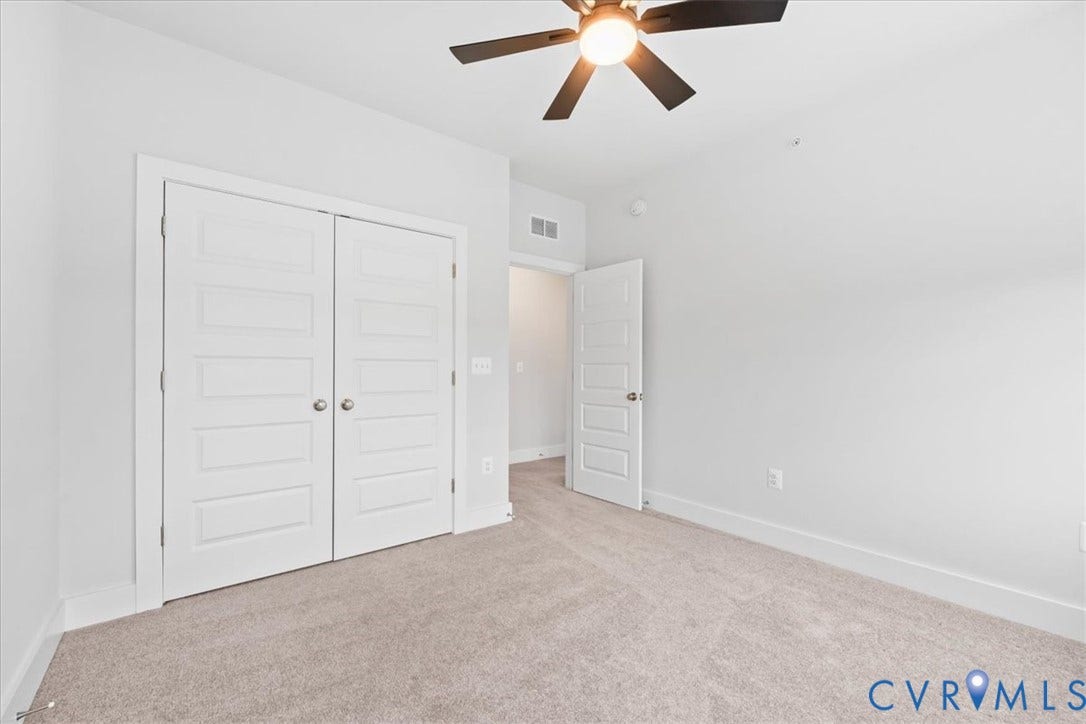 Neutral-toned carpeting, ceiling fan with integrated lighting, and multiple paneled doors