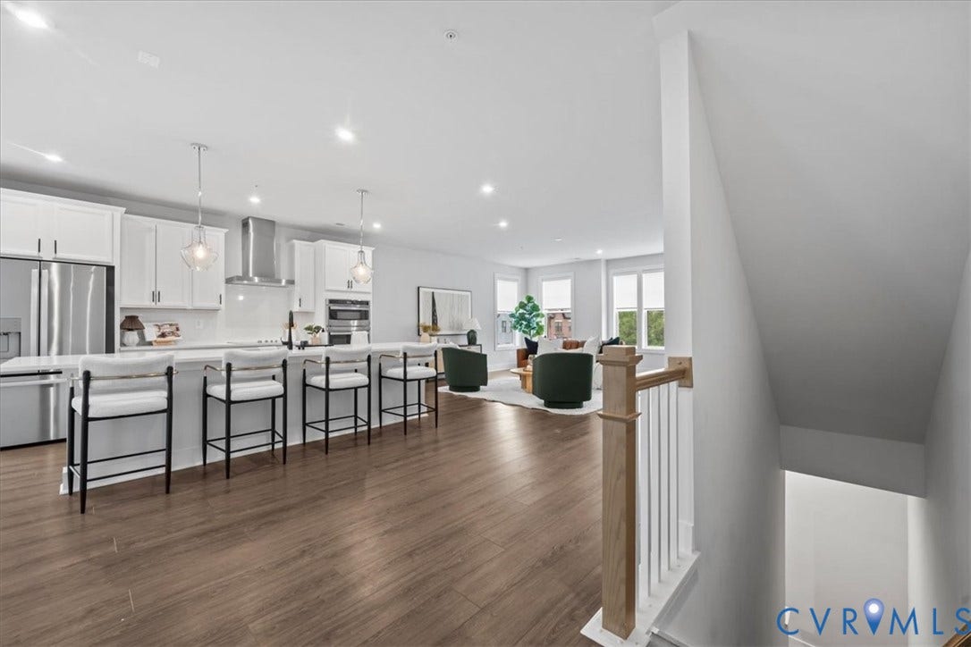 Open-concept living space featuring wood-finish flooring, white cabinetry, stainless steel appliances, and a kitchen island with pendant lighting