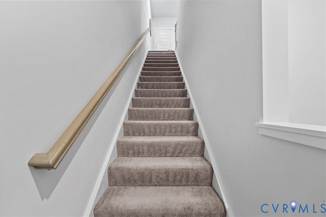 Carpeted staircase with light-toned wood-finish handrail and crisp white trim