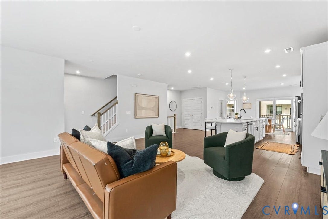 Open-concept living area featuring wood-finish flooring, recessed lighting, a white kitchen island with pendant lighting, and a staircase with white balusters