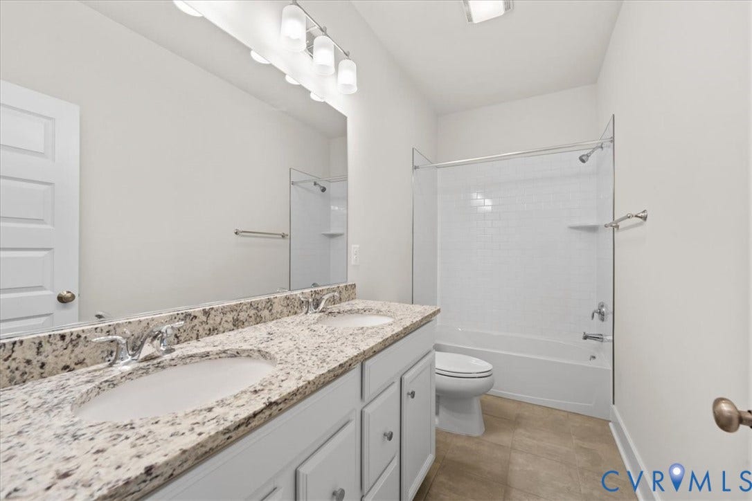 Dual basin vanity with stone countertop, white shaker cabinetry, chrome fixtures, and a subway tile shower surround