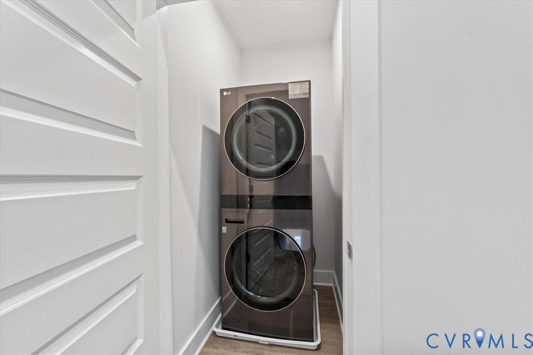 Stackable washer and dryer unit, white walls, and wood-finish flooring