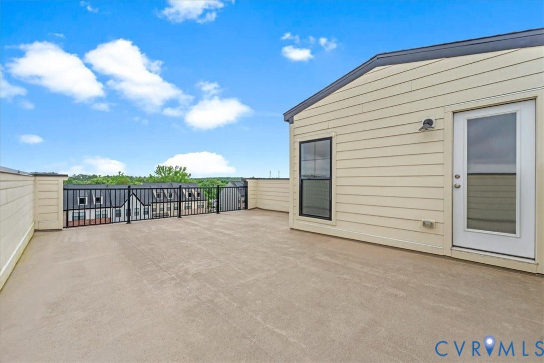 Expansive rooftop deck featuring a concrete surface, black metal railing, and light-colored siding