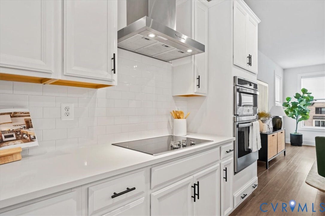 White shaker-style cabinetry, stainless steel range hood, built-in double ovens, white subway tile backsplash, and light-toned countertops