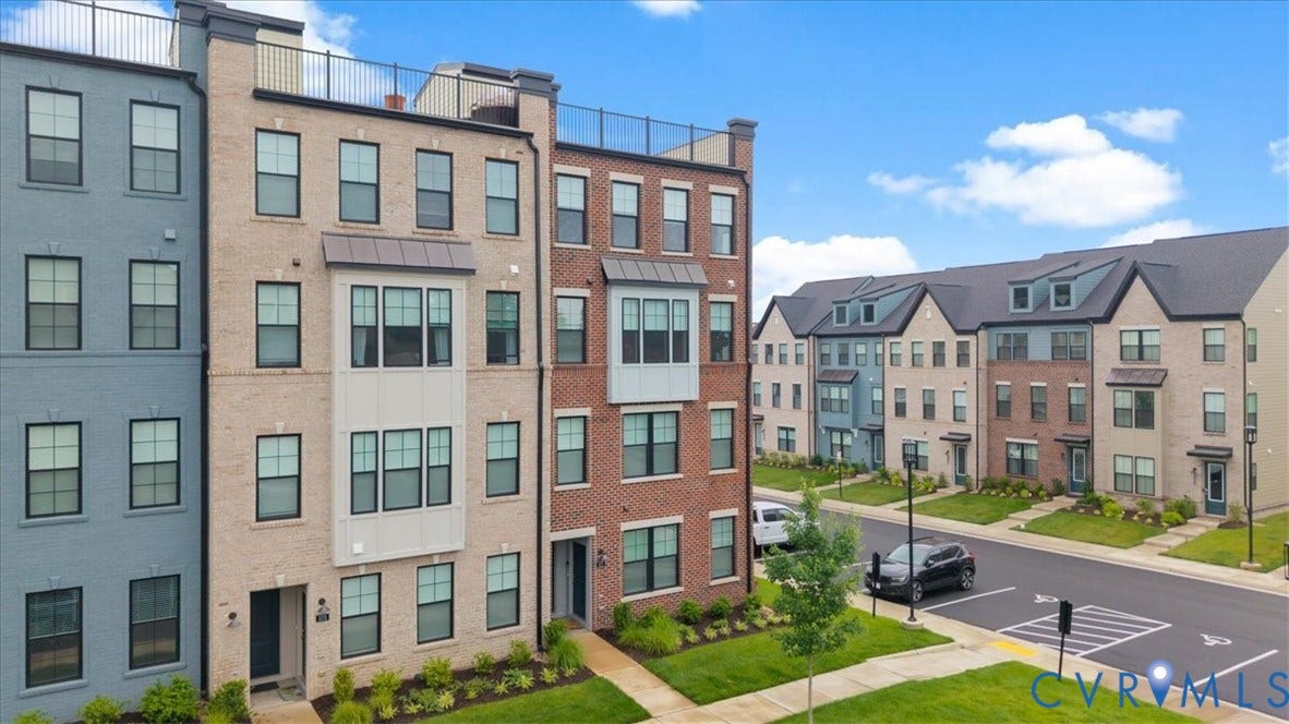 Contemporary townhome featuring a brick facade, multi-pane windows, front landscaping, and a rooftop deck with metal railing