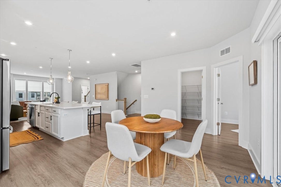 Open-concept living space featuring wood-finish flooring, recessed lighting, a kitchen island with pendant lighting, and a pantry with wire shelving