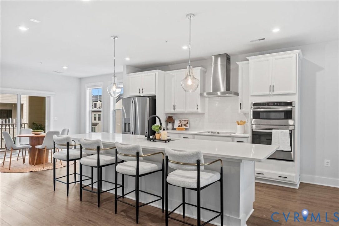 Spacious kitchen featuring an extended island with seating, white shaker cabinetry, stainless steel appliances, and a tile backsplash
