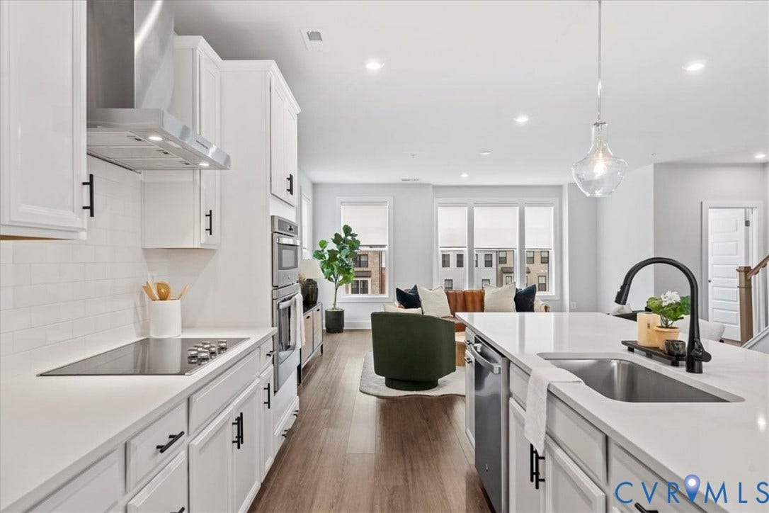 White shaker cabinetry with black hardware, stainless steel appliances, recessed lighting, wood-finish flooring, and a kitchen island with an undermount sink