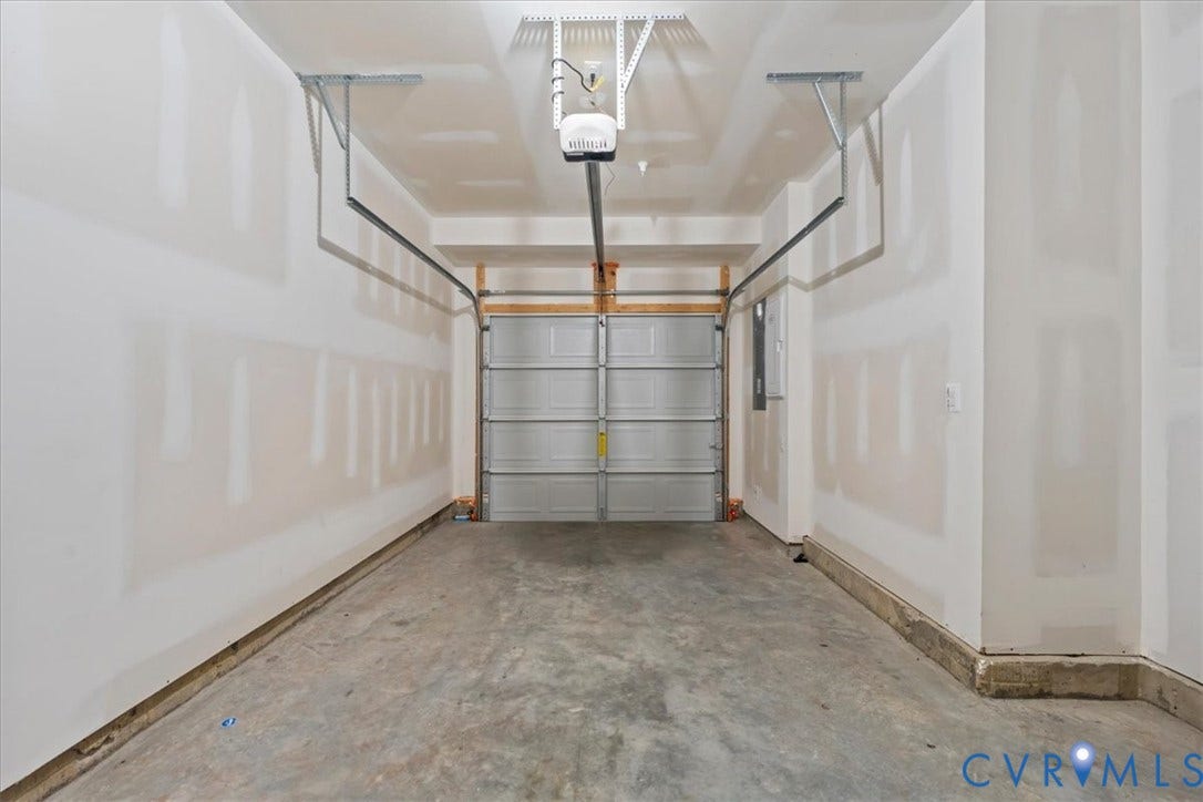 Attached garage with a concrete floor, equipped with an automatic garage door opener and overhead storage brackets