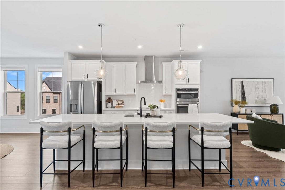 Expansive kitchen island with seating, white shaker cabinetry, stainless steel appliances, pendant lighting, and wood-finish flooring