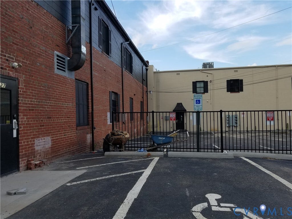 Brick exterior with upper-level dark siding, ground-level entry, and a paved parking lot with marked spaces