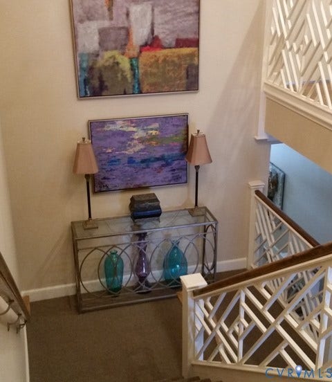 Decorative console table with a glass top, carpeted stairs, and a white geometric-patterned stair railing