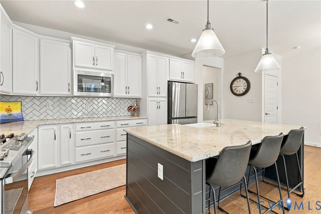 Kitchen featuring white cabinetry, stainless steel appliances, herringbone tile backsplash, and a center island with a stone-finish countertop