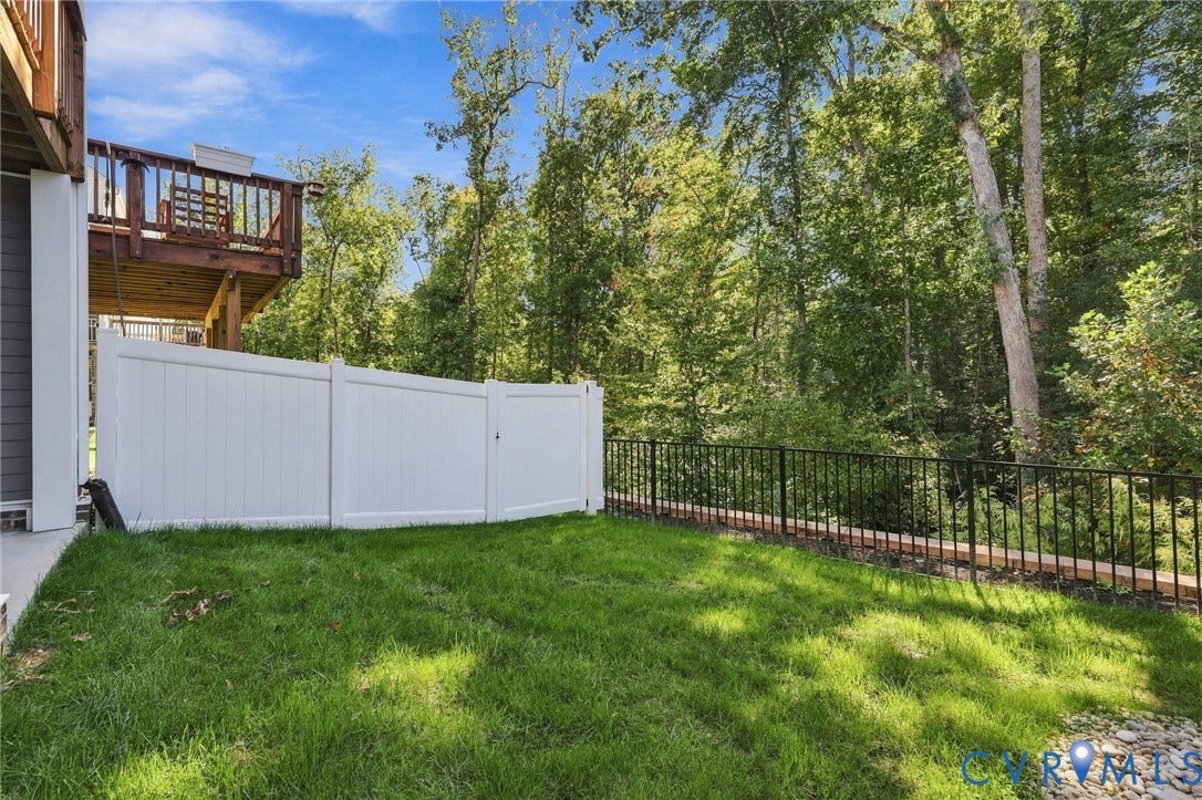 Expansive grassy yard with a white privacy fence, black metal railing, and mature trees
