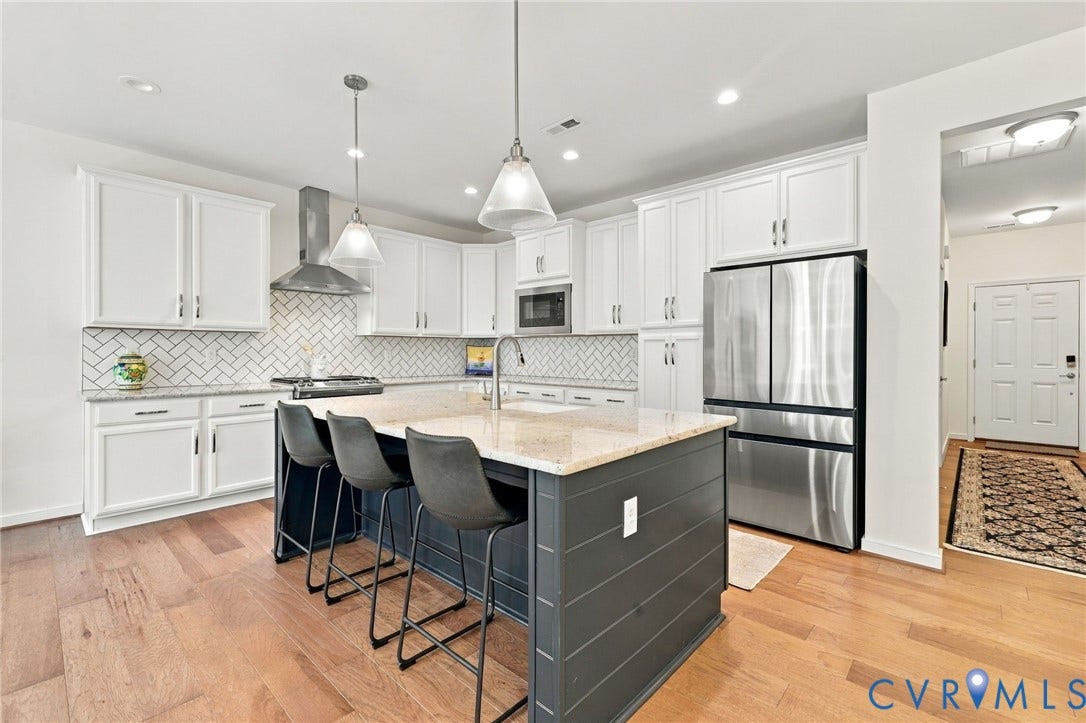 Gourmet kitchen featuring a central island with bar seating, stainless steel appliances, herringbone tile backsplash, wood-finish flooring, and pendant lighting