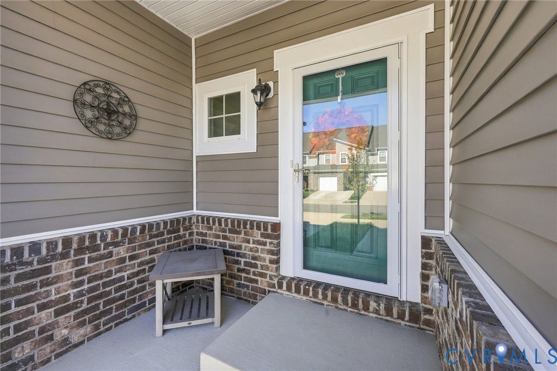 Entryway featuring a storm door, sconce lighting, durable siding, and brick detailing
