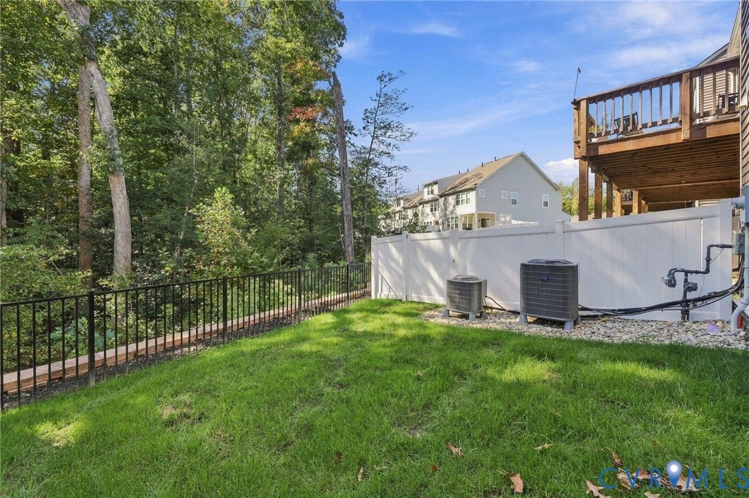 Expansive backyard featuring a manicured lawn, a white privacy fence, and a black metal fence bordering a wooded area