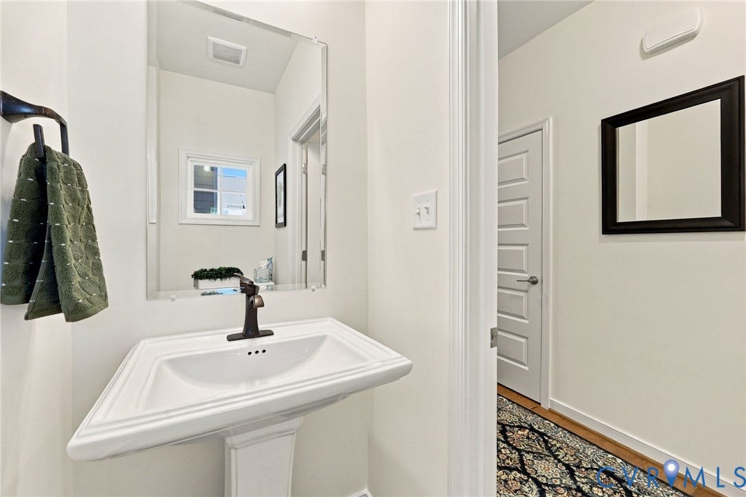 Pedestal sink with bronze-finish faucet, rectangular wall-mounted mirror, and wood-finish flooring