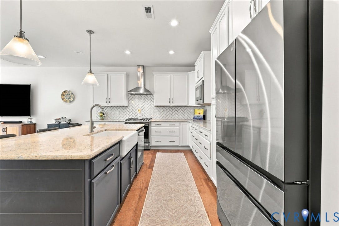 Stainless steel appliances, wood-finish flooring, white cabinetry, farmhouse sink, and a herringbone tile backsplash