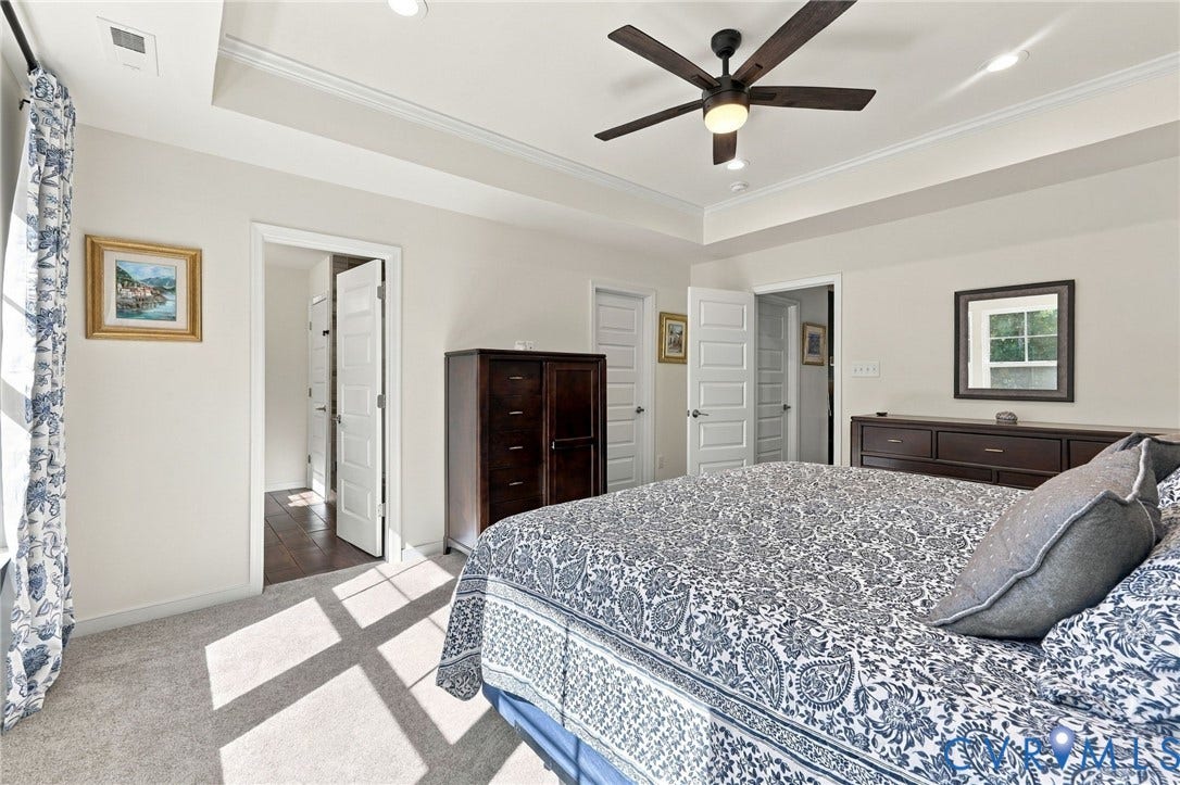 Tray ceiling with crown molding, ceiling fan with integrated lighting, carpeted flooring, and white paneled doors
