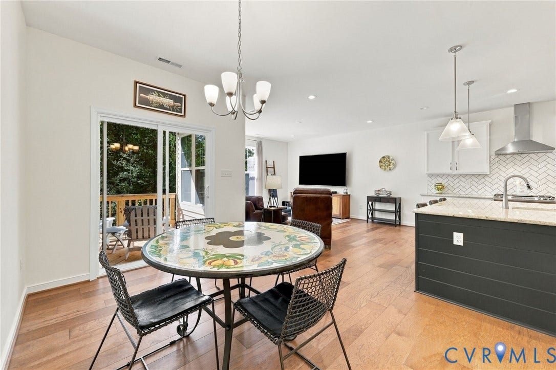 Open-concept living space featuring wood-finish flooring, a kitchen island with stone countertops, white cabinetry, a herringbone tile backsplash, and a sliding glass door leading to an outdoor deck