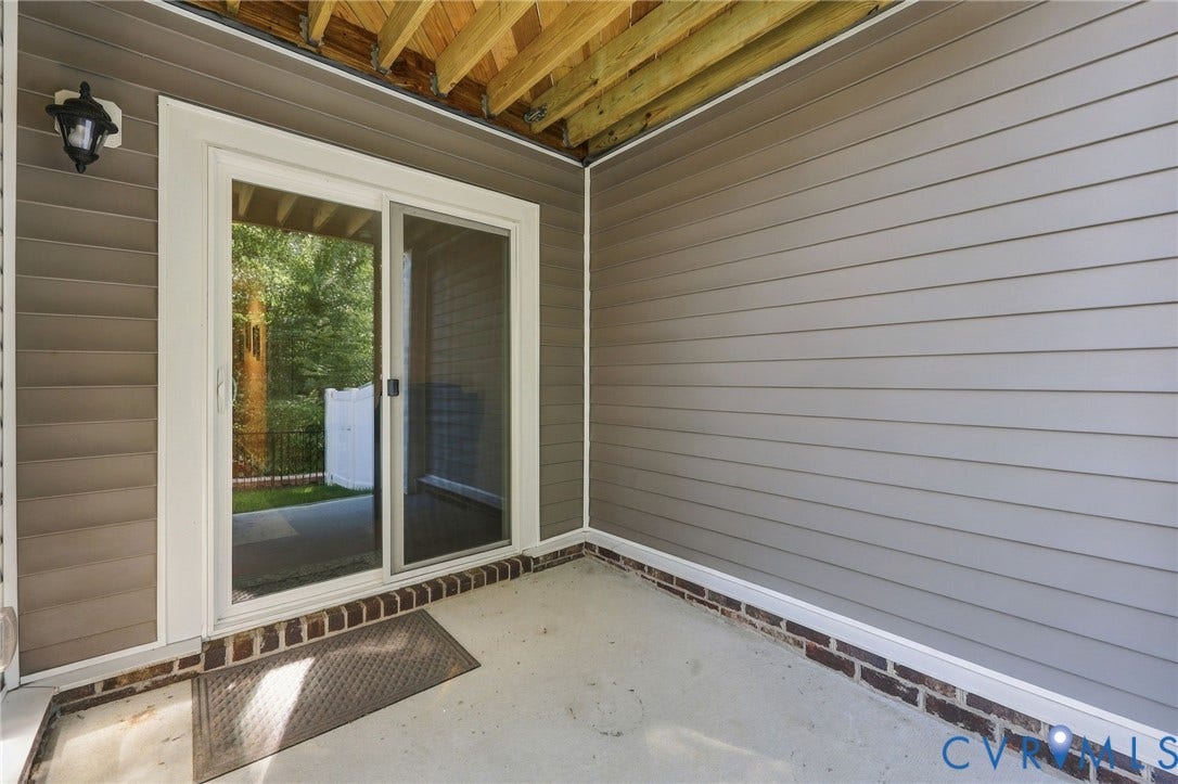 Covered outdoor patio with a concrete floor, light gray siding, and exposed brick detailing