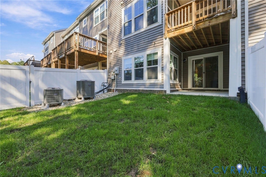 Expansive grassy area featuring a white privacy fence, two exterior AC units, a ground-level patio, and a sliding glass door