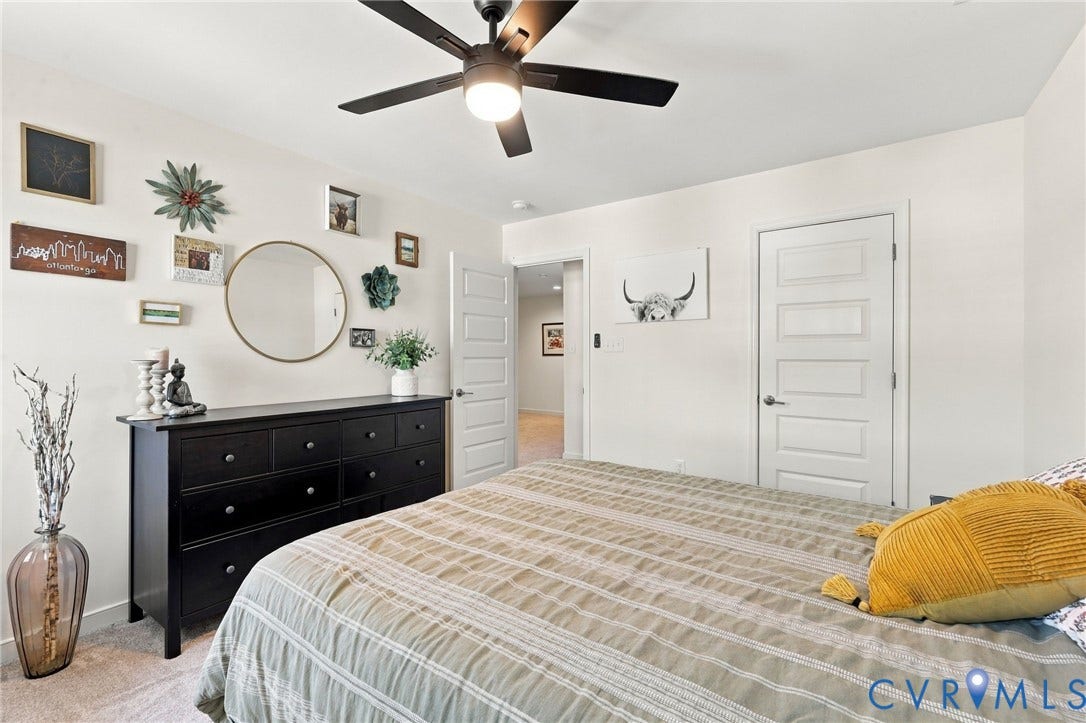 Primary bedroom featuring neutral striped bedding, black six-drawer dresser with circular mirror, ceiling fan with integrated lighting, white panel doors, and neutral carpeting throughout
