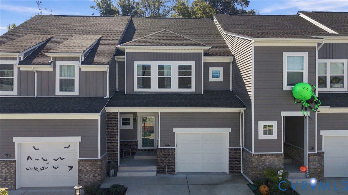 Gray siding exterior with white trim, dark shingle roof, two white garage doors, and brick accents