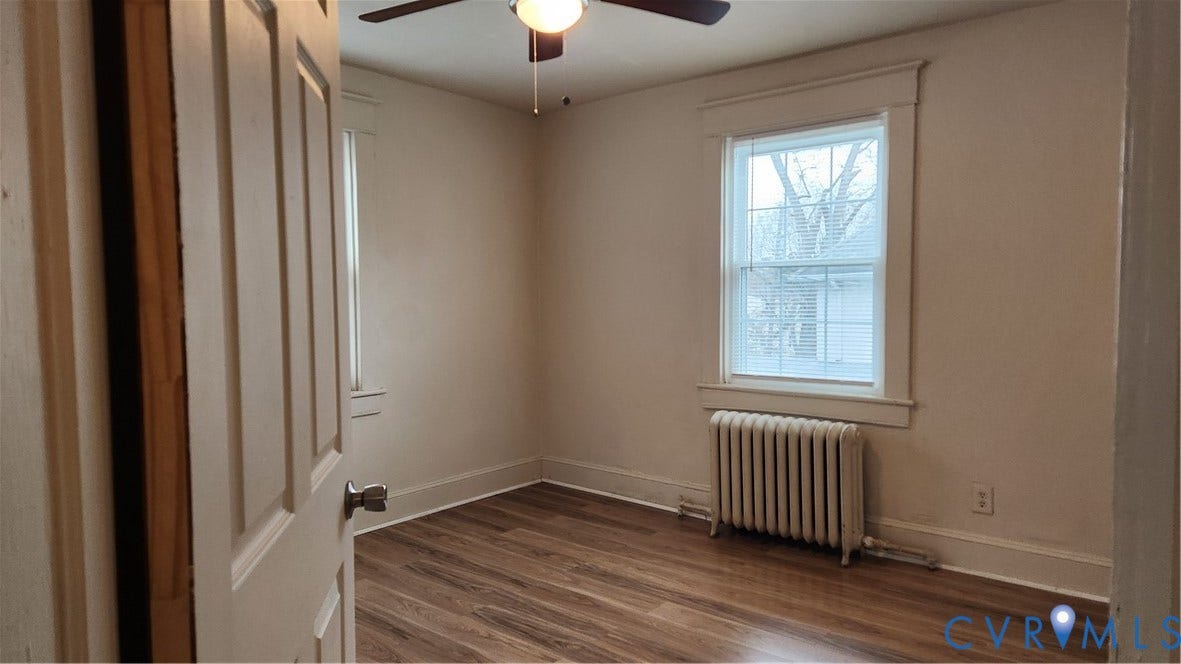 Wood-finish flooring, ceiling fan with integrated lighting, and a window with a radiator below