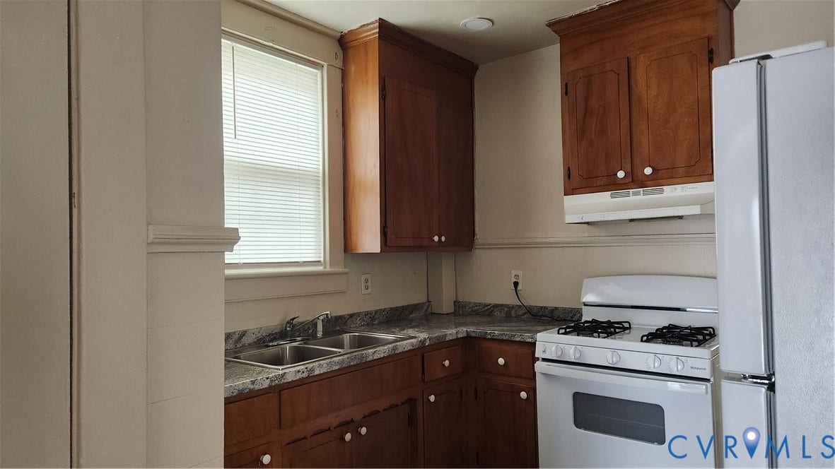 Kitchen featuring wood cabinetry, a double basin sink, a gas range, a white refrigerator, and a window with blinds