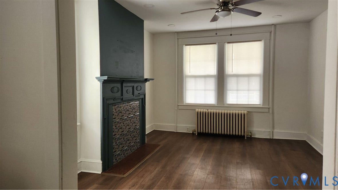 Wood-finish flooring, decorative fireplace with tile insert, two large windows, ceiling fan with integrated lighting, and recessed lighting