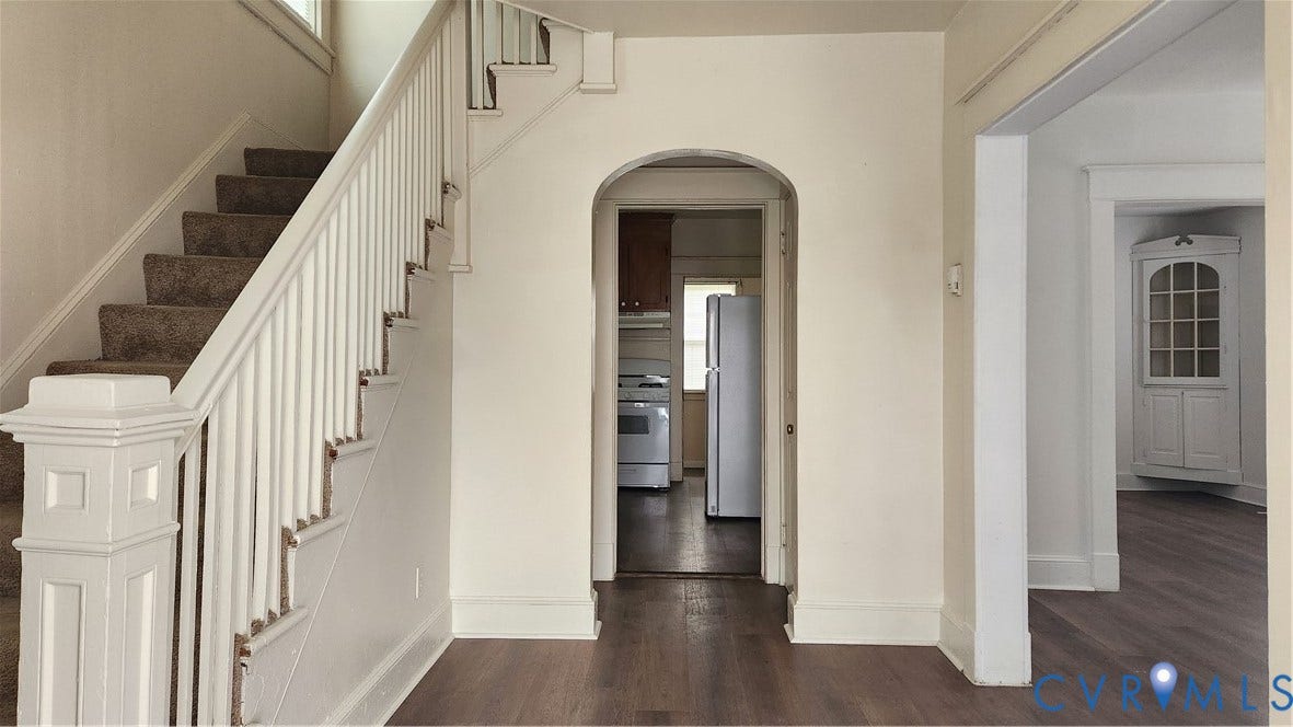Hardwood flooring, painted white staircase with carpeted treads, arched doorway, built-in corner cabinet, and white appliances