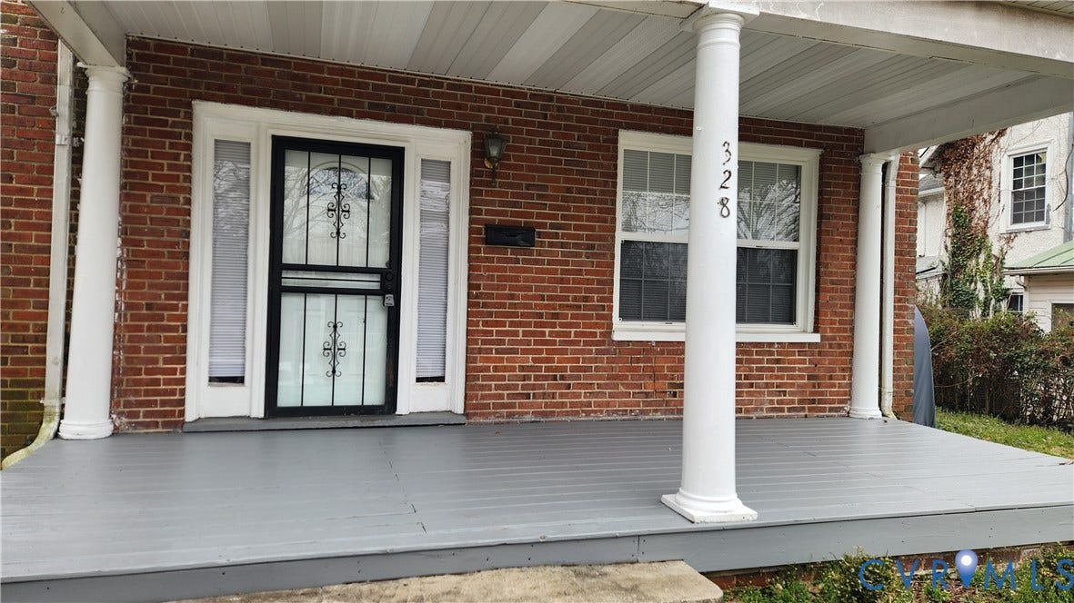 Brick exterior with white trim, front porch with gray decking, white columns, and a storm door with decorative ironwork