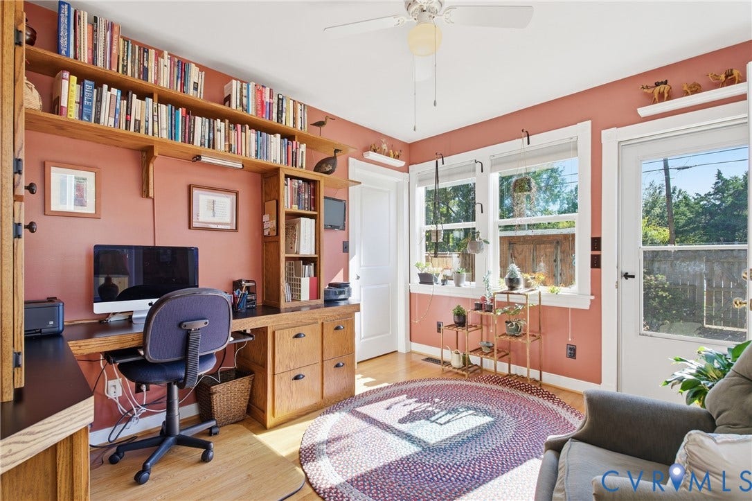 Built-in desk with integrated shelving, hardwood-finish flooring, multiple windows, ceiling fan, and a glass-paneled exterior door