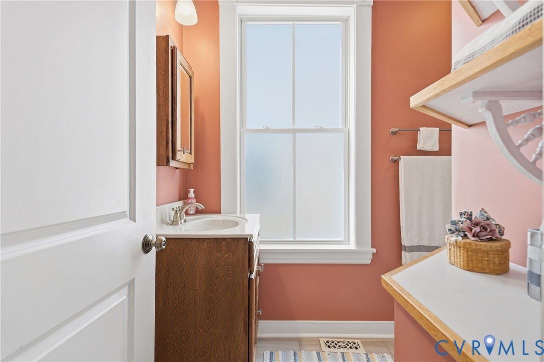 Bathroom featuring a wood-finish vanity with a white countertop and basin sink, a frosted window, and built-in shelving