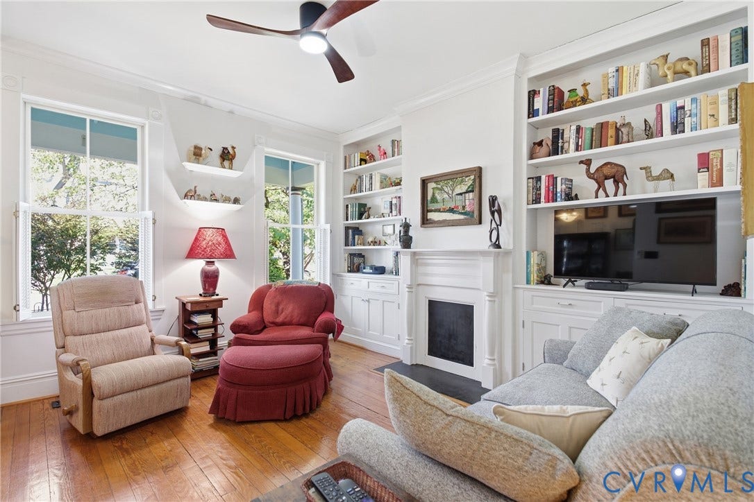 Wood-finish flooring, two large windows, built-in shelving, a fireplace, and a ceiling fan with integrated lighting