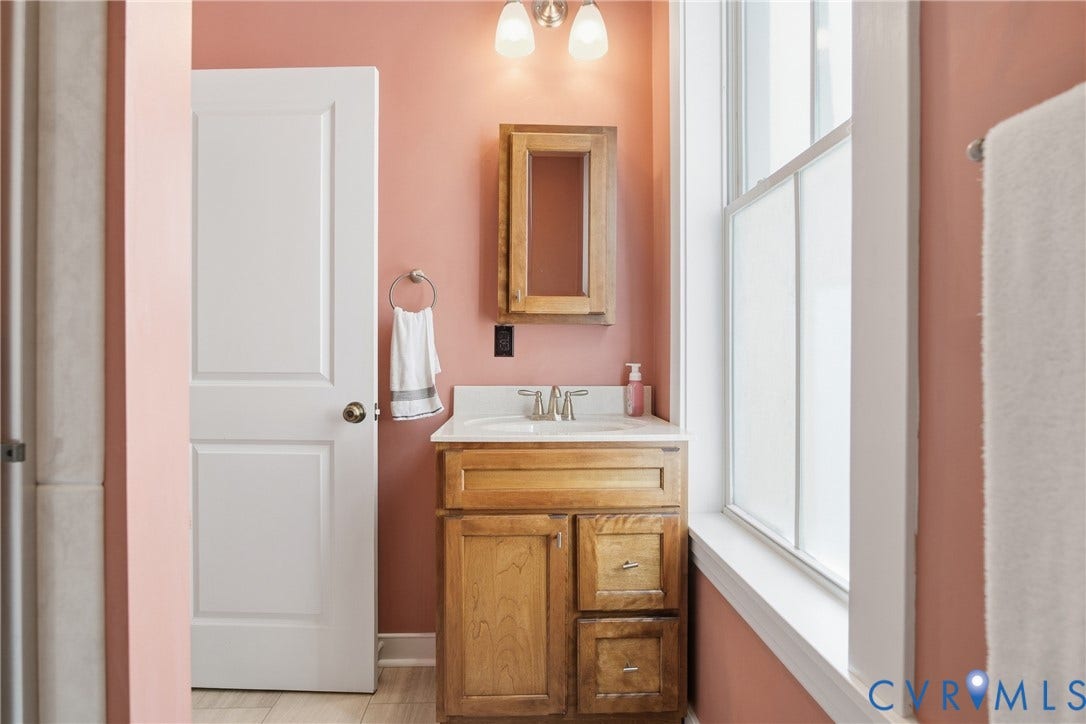 Wood-finish vanity with white countertop, integrated sink, and wall-mounted light fixture