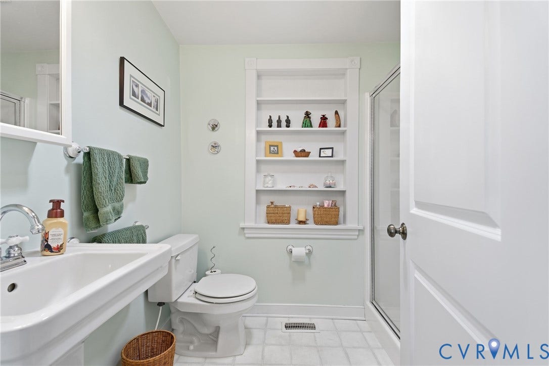 Pedestal sink with chrome faucet, built-in shelving, white paneled door, and a walk-in shower with a glass enclosure