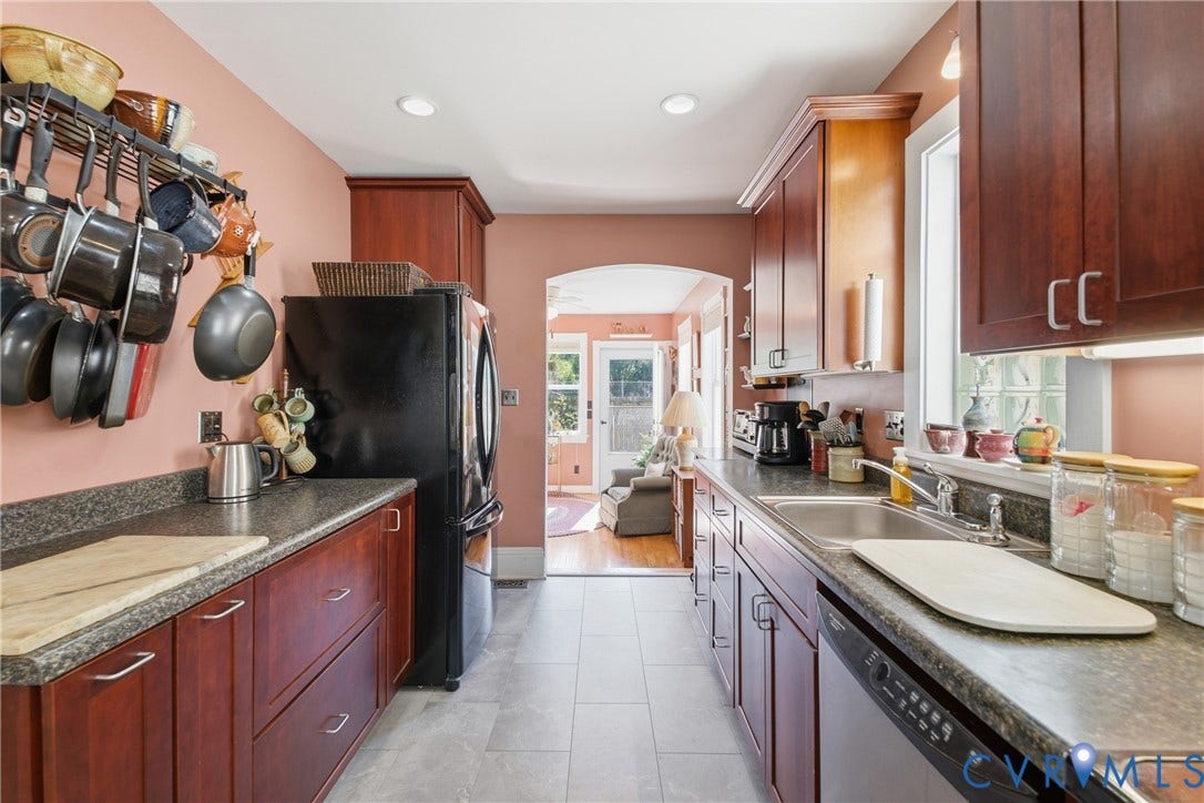 Galley kitchen featuring wood-finish cabinetry, dark countertops, a black refrigerator, a stainless steel sink, and tile flooring