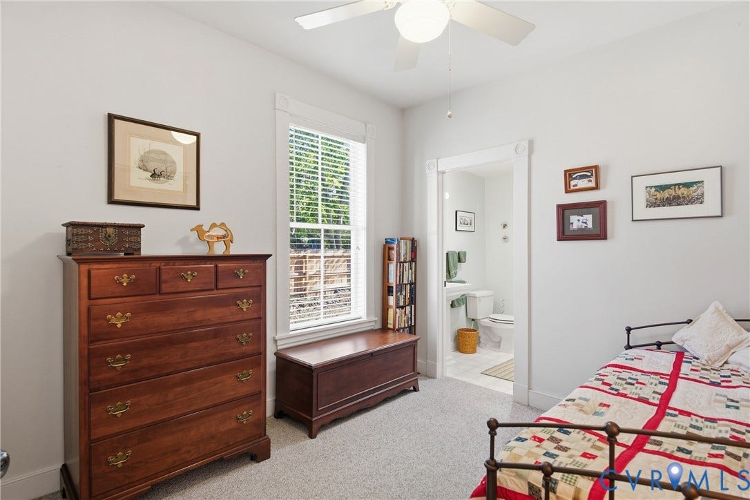 Recessed window with blinds, ceiling fan with light fixture, light-toned carpet flooring, white door frame with decorative trim, and white walls