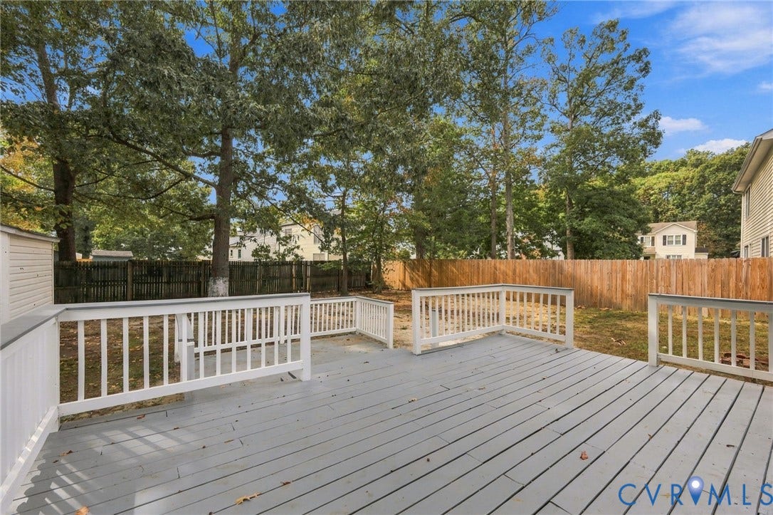 5831 Larrymore Road, Richmond, VA 23225 Elevated rear deck with white wood-style railings, spanning a private backyard enclosed by a tall wood privacy fence and mature trees