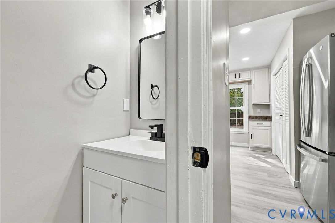 5831 Larrymore Road, Richmond, VA 23225 Powder room featuring a white vanity cabinet, rectangular countertop sink, matte black hardware, and an arched mirror
